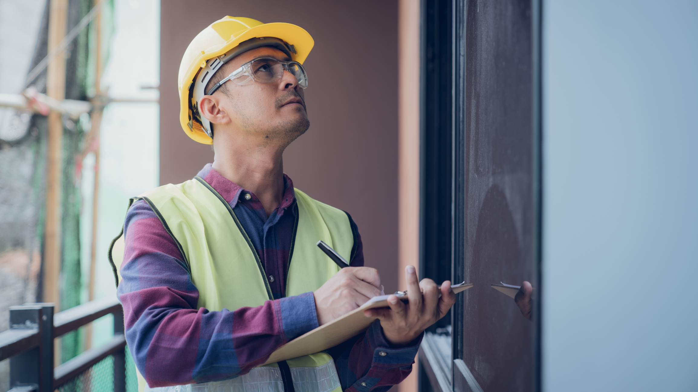 Male inspector with a clipboard looking up at a building.