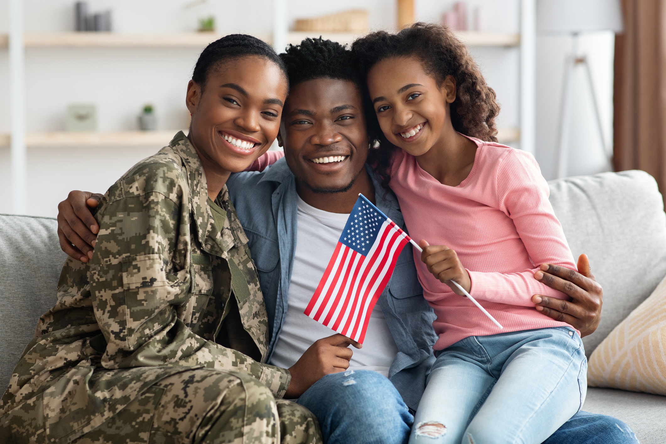 Military family smiling together on couch holding American flag