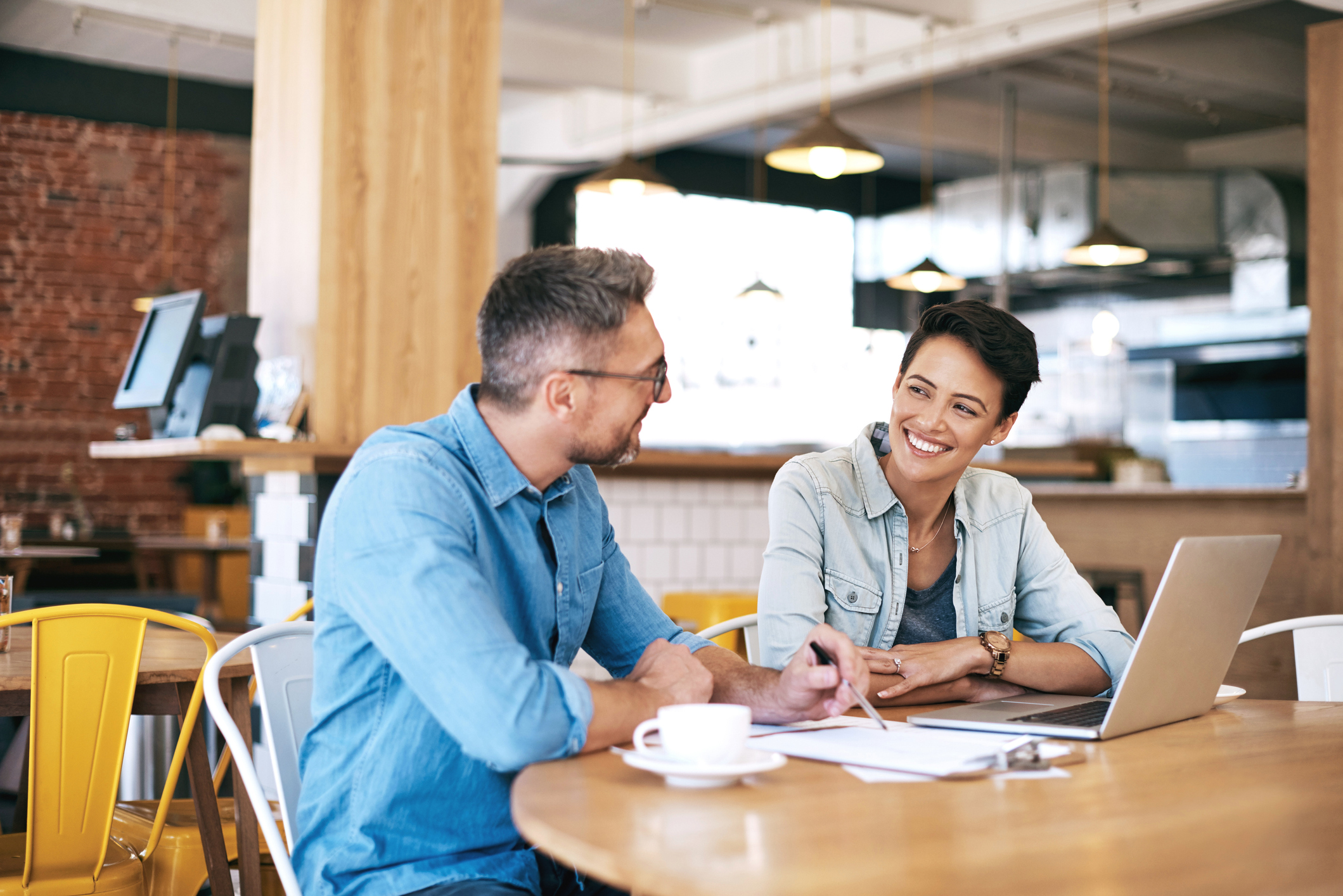 Man and woman going over paperwork and using a laptop together in a coffee shop