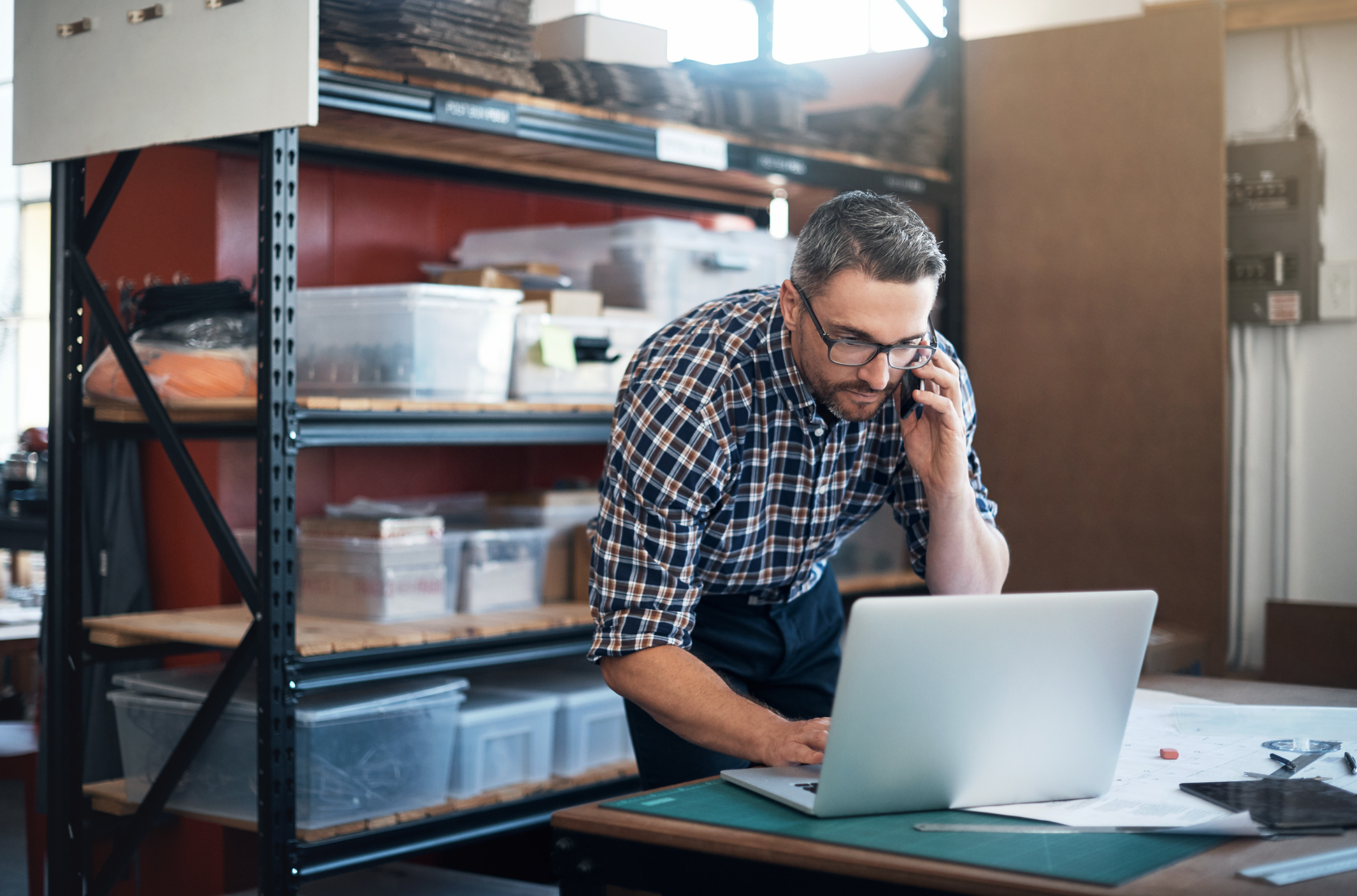 Man using a laptop and mobile phone in a workshop.